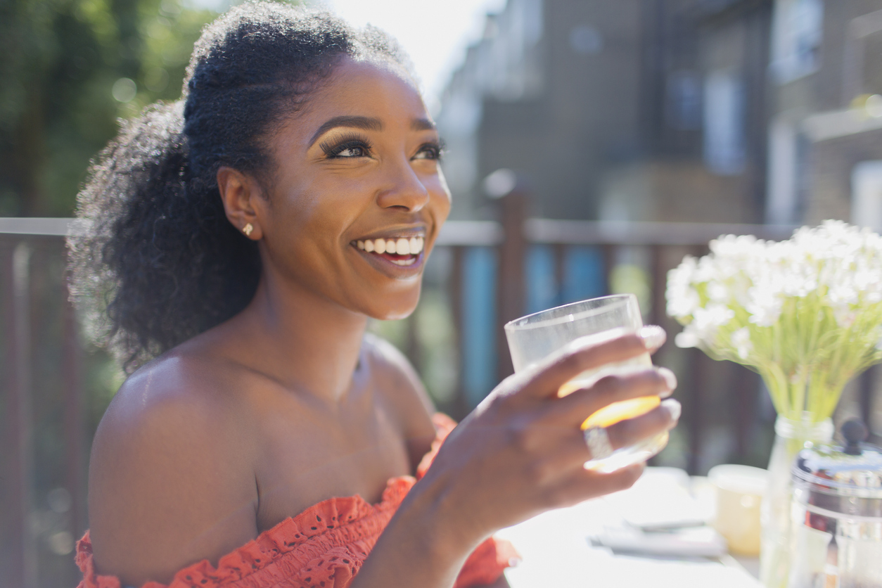 Happy young woman drinking orange juice on sunny balcony